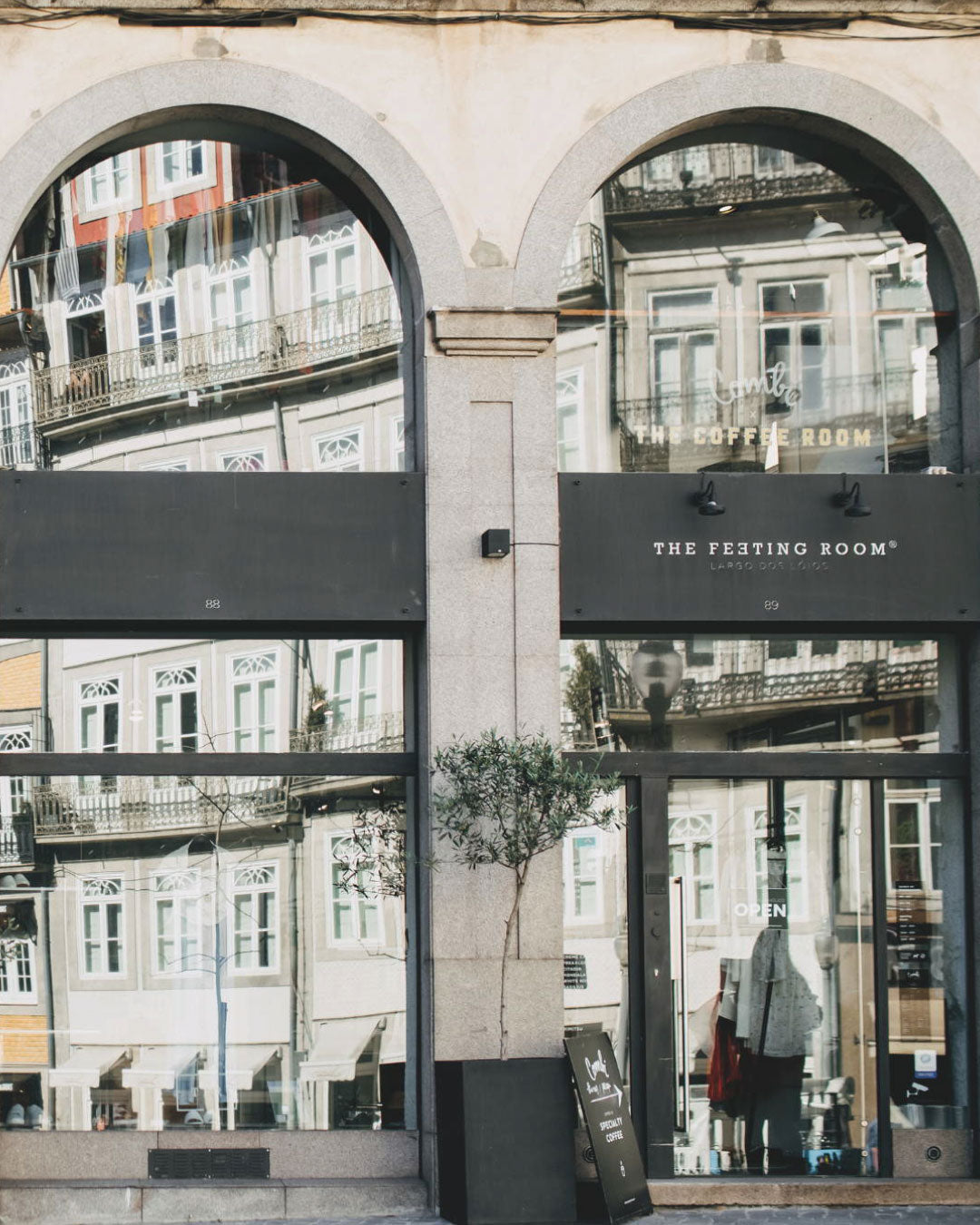 Arched glass shopfront of The Feeting Room Lóios concept store, reflecting the historic buildings of Largo dos Lóios, Porto